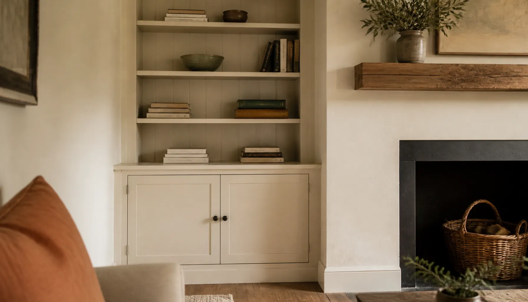 Living room alcoves either side of a fireplace fitted with cream painted cabinets below and open shelves above holding books and pottery