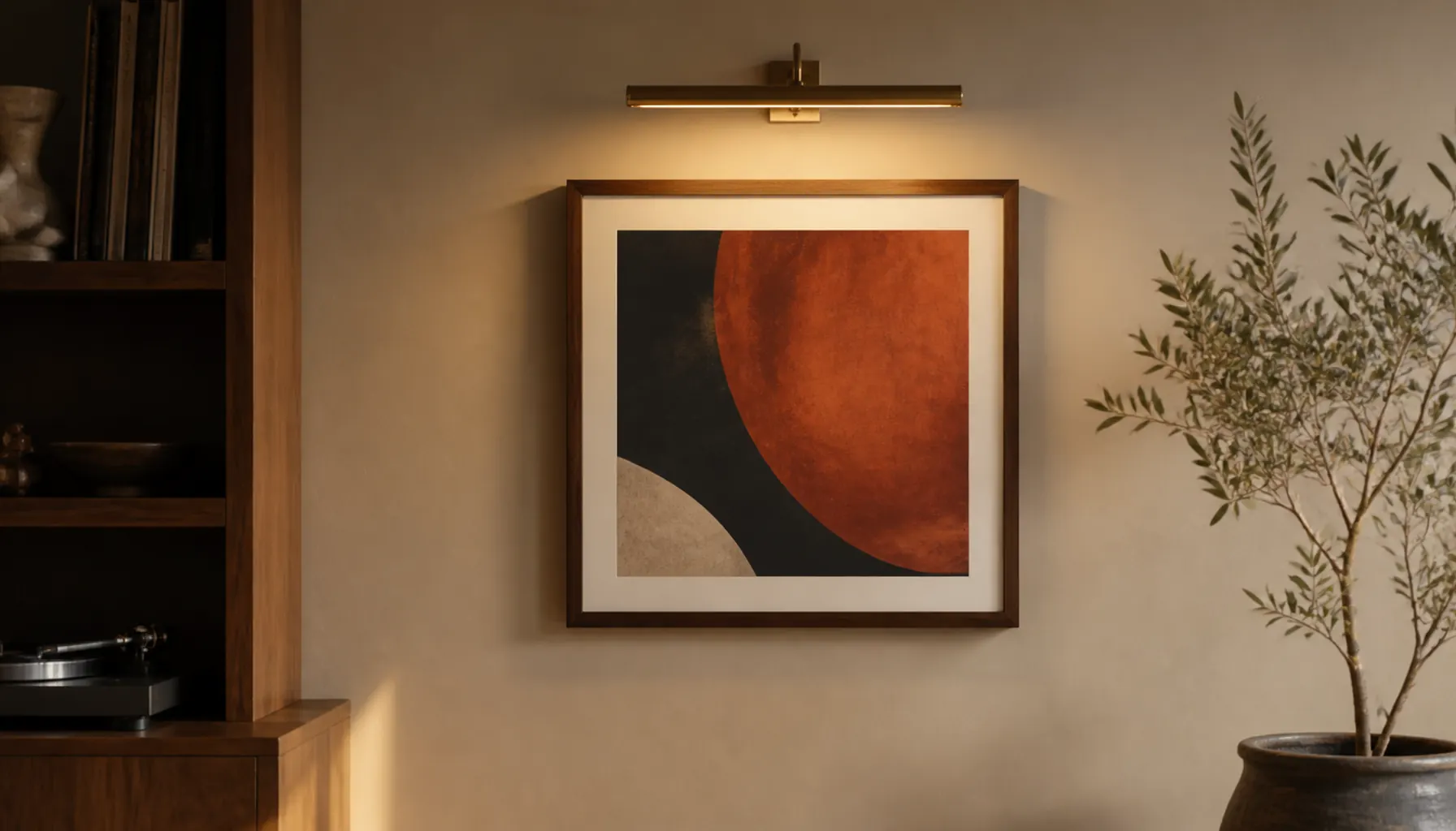 A framed album sleeve on a sand-colored wall lit from above by a slim picture light with no glare on the glass
